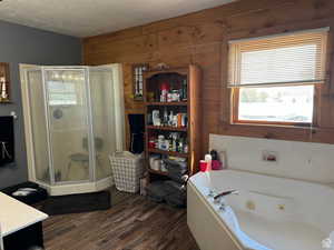 Bathroom featuring wooden walls, a stall shower, wood finished floors, vanity, and a whirlpool tub
