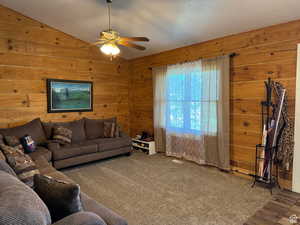 Living room featuring a ceiling fan, wooden walls, and vaulted ceiling