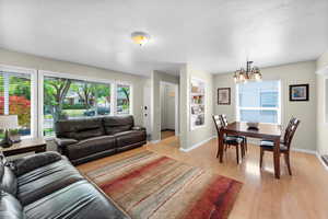 Living area featuring a chandelier, light wood-style flooring, baseboards, and a textured ceiling
