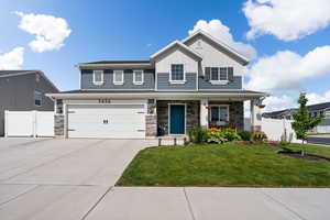 View of front of property with driveway, board and batten siding, an attached garage, covered porch, and stone siding