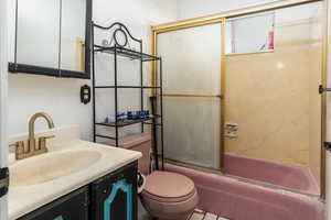 Bathroom featuring toilet, shower / bath combination with glass door, and vanity