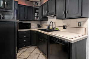 Kitchen with black appliances, a sink, tasteful backsplash, light tile patterned floors, and glass insert cabinets