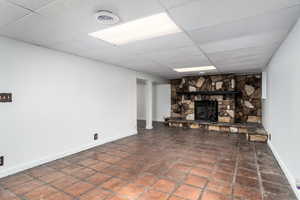 Finished basement featuring a stone fireplace, baseboards, and a drop ceiling