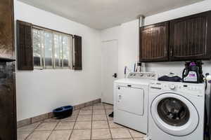 Laundry area with cabinet space, independent washer and dryer, light tile patterned floors, and baseboards