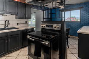 Kitchen featuring stainless steel range with electric cooktop, tile counters, light tile patterned floors, a ceiling fan, and a sink