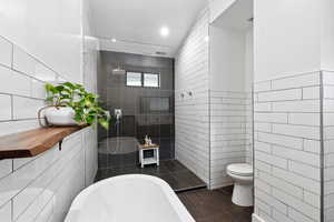 Bathroom featuring tile walls, a freestanding tub, toilet, tile patterned flooring, and walk in shower