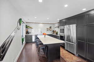 Kitchen with appliances with stainless steel finishes, open shelves, light countertops, a kitchen island, and decorative backsplash