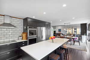 Kitchen featuring wall chimney range hood, stainless steel appliances, light countertops, a center island, and decorative backsplash