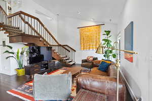 Living room with stairs, baseboards, wood finished floors, lofted ceiling, and recessed lighting
