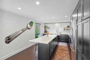 Kitchen with open shelves, a center island, freestanding refrigerator, backsplash, and a breakfast bar area