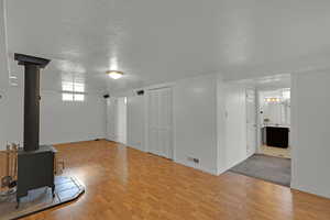 Unfurnished living room with wood finished floors, a wood stove, a textured ceiling, and baseboards