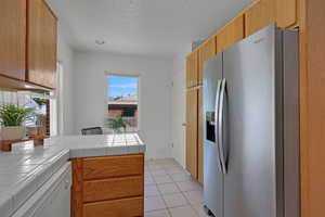 Kitchen featuring stainless steel fridge with ice dispenser, white dishwasher, tile countertops, a textured ceiling, and light tile patterned flooring