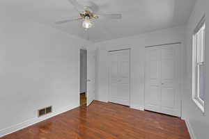 Unfurnished bedroom with two closets, dark wood-style flooring, baseboards, and a ceiling fan