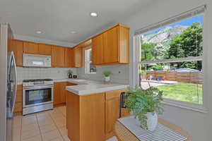 Kitchen with appliances with stainless steel finishes, backsplash, a peninsula, light tile patterned flooring, and healthy amount of natural light