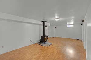 Below grade area with light wood-style floors, a wood stove, a textured ceiling, and baseboards