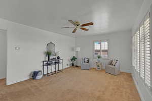 Living area with a ceiling fan, light colored carpet, and baseboards