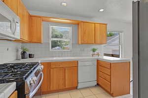 Kitchen with white appliances, a sink, healthy amount of natural light, tasteful backsplash, and a textured ceiling