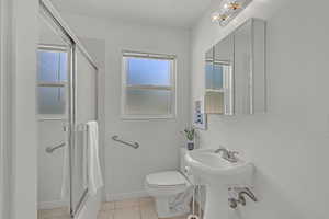 Full bath with a shower with door, tile patterned floors, toilet, baseboards, and a sink