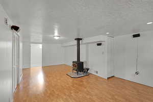 Below grade area with a textured ceiling, light wood finished floors, a wood stove, and baseboards