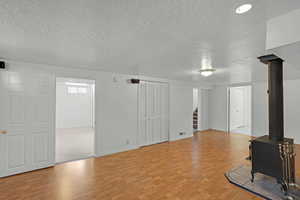 Unfurnished living room featuring a textured ceiling, wood finished floors, stairway, a wood stove, and baseboards