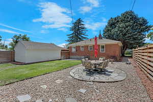Back of property featuring an outbuilding, a chimney, brick siding, a patio, and roof with shingles