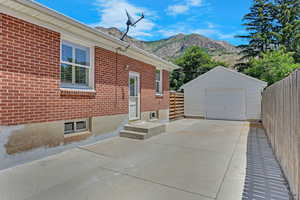 View of property exterior with a mountain view, concrete driveway, a garage, an outdoor structure, and brick siding