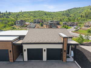 View of front of property featuring a wooded view, an attached garage, driveway, and a shingled roof