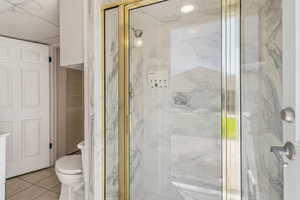 Bathroom with a marble finish shower, tile patterned floors, toilet, and a closet