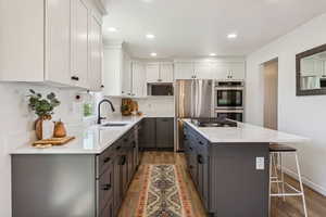 Kitchen with a sink, stainless steel appliances, gray cabinets, wood finished floors, and a kitchen island