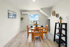 Dining space featuring a wall mounted AC, light wood-style flooring, baseboards, and recessed lighting