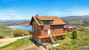 Rear view of property with a deck with water view, a chimney, driveway, a garage, and a shingled roof
