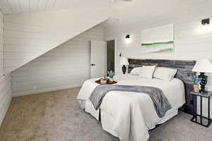 Bedroom with carpet floors, wood walls, and vaulted ceiling