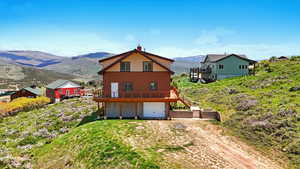 Back of property featuring a garage, a chimney, a deck with mountain view, and driveway