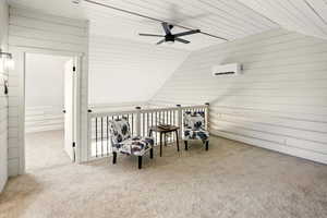Living area with vaulted ceiling, wood walls, ceiling fan, carpet floors, and a wall unit AC