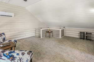 Additional living space with a wall mounted AC, wood walls, lofted ceiling, and carpet floors