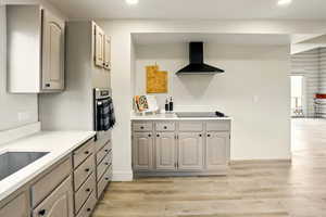 Kitchen featuring wall chimney range hood, recessed lighting, light wood finished floors, black electric cooktop, and baseboards