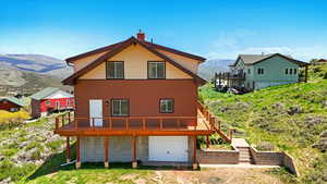 Back of property with a chimney, a deck with mountain view, a garage, driveway, and stairway