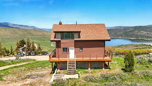 Rear view of property with a deck with water view, a chimney, stairs, and roof with shingles