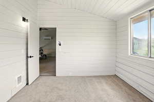 Carpeted empty room with lofted ceiling and wooden walls