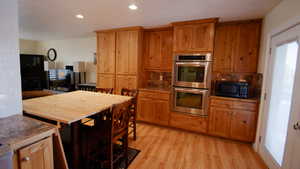 Kitchen featuring double oven, light wood finished floors, brown cabinetry, recessed lighting, and decorative backsplash
