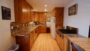 Kitchen with stainless steel appliances, a sink, light wood finished floors, recessed lighting, and decorative backsplash