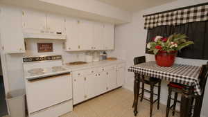 Kitchen with electric stove, extractor fan, light countertops, and white cabinetry