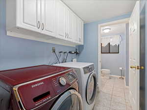 Laundry area with cabinet space, separate washer and dryer, light tile patterned flooring, and baseboards