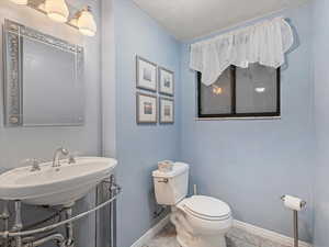Half bathroom with baseboards, toilet, a sink, a textured ceiling, and tile patterned floors