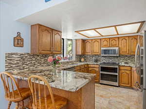 Kitchen with appliances with stainless steel finishes, a peninsula, brown cabinetry, and a sink
