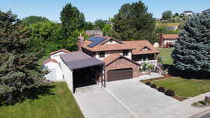 View of front facade featuring a front lawn, roof mounted solar panels, brick siding, a chimney, and concrete driveway