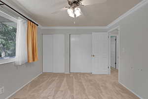Unfurnished bedroom with two closets, light carpet, crown molding, a textured ceiling, and a ceiling fan