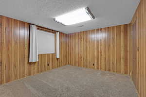 Carpeted spare room with a textured ceiling and wooden walls