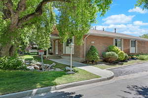 View of property hidden behind natural elements featuring brick siding, a front lawn, and a shingled roof