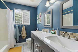 Bathroom with toilet, shower / tub combo with curtain, double vanity, marble look tile flooring, and baseboards